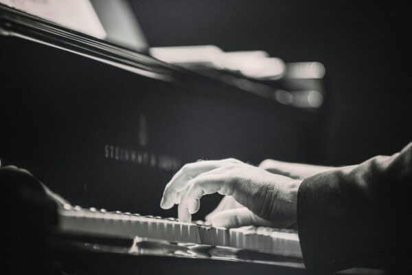 Black-and-white close-up of hands playing piano beneath a microphone