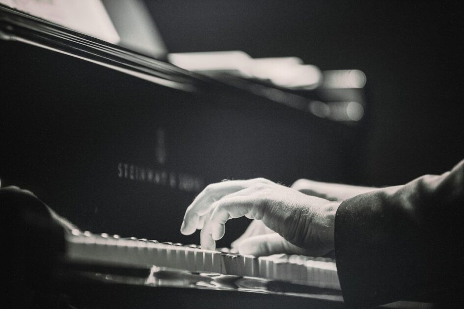 Black-and-white close-up of hands playing piano beneath a microphone